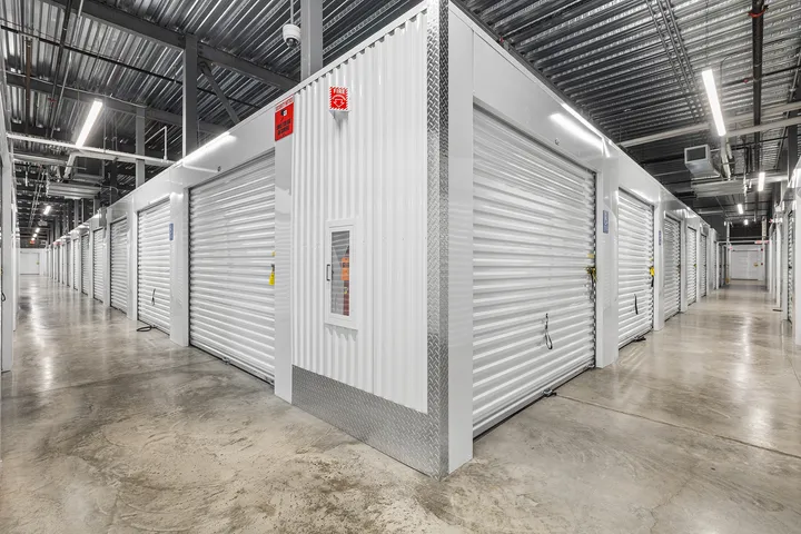 Indoor storage facility hallway featuring rows of white roll-up doors and polished concrete floors
