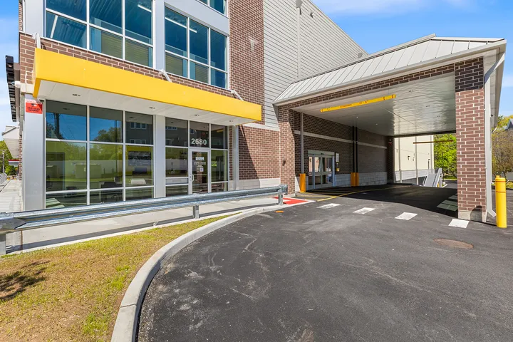 Multi-story brick facility entrance featuring large glass windows, a yellow awning, and a covered drive-in loading bay