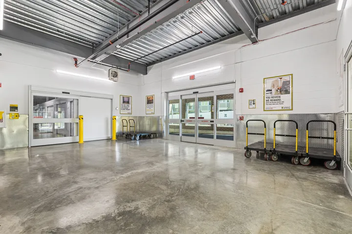 Indoor loading area with sliding glass doors, concrete floors, moving carts, and diamond plate wall guards