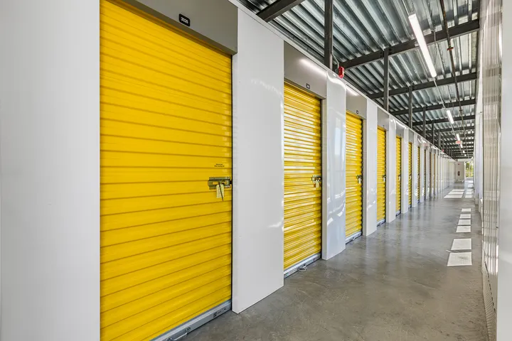 Bright yellow roll-up doors line a long, well-lit indoor self-storage hallway with concrete floors